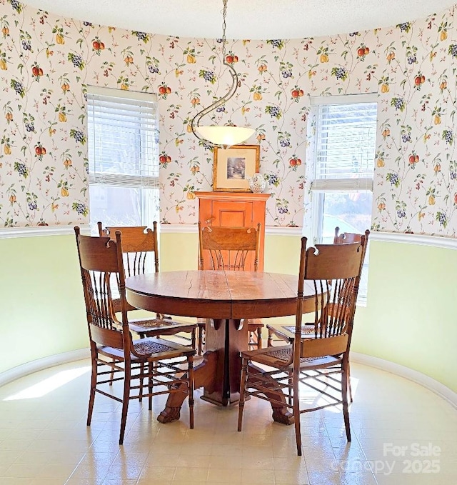 dining area featuring baseboards, a textured ceiling, wainscoting, and wallpapered walls