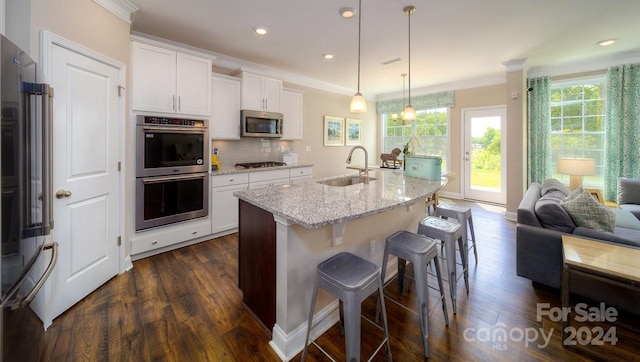 kitchen with hanging light fixtures, an island with sink, white cabinetry, stainless steel appliances, and sink