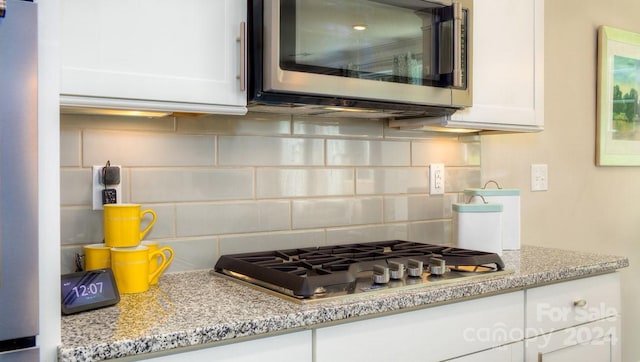 kitchen with light stone countertops, decorative backsplash, white cabinetry, and stainless steel appliances