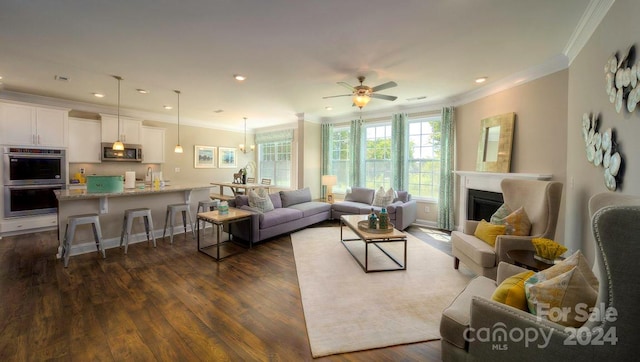 living room featuring ornamental molding, dark wood-type flooring, and ceiling fan with notable chandelier