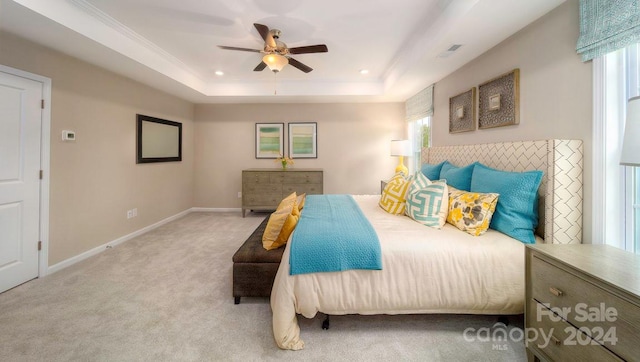 carpeted bedroom featuring ceiling fan, multiple windows, and a raised ceiling