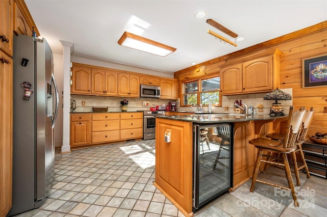 kitchen with decorative backsplash, a kitchen breakfast bar, wooden walls, beverage cooler, and appliances with stainless steel finishes