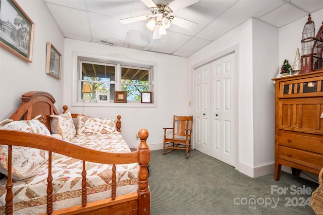 carpeted bedroom with a closet, a paneled ceiling, and ceiling fan