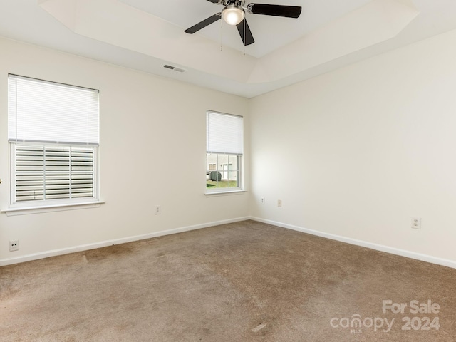 carpeted spare room featuring a tray ceiling and ceiling fan