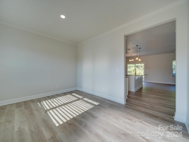 empty room with light wood-type flooring, crown molding, and an inviting chandelier