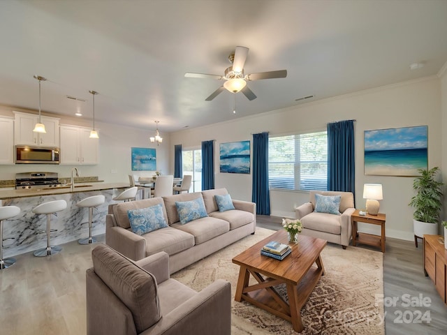 living room featuring ceiling fan with notable chandelier, light hardwood / wood-style flooring, sink, and crown molding