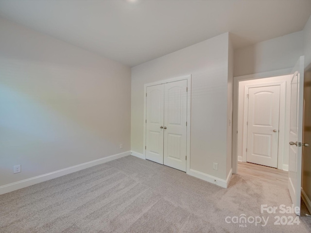 unfurnished bedroom with light colored carpet and a closet