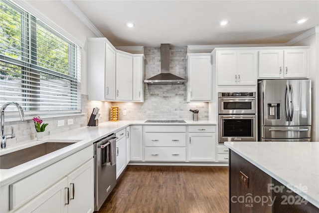 kitchen featuring wall chimney range hood, sink, white cabinetry, stainless steel appliances, and crown molding