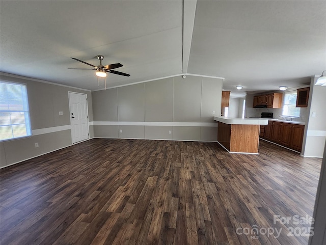 unfurnished living room featuring dark wood-type flooring, a ceiling fan, crown molding, and a sink