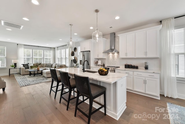 kitchen with a kitchen island with sink, hardwood / wood-style flooring, wall chimney exhaust hood, a breakfast bar area, and stainless steel appliances