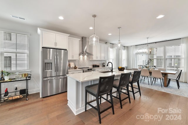 kitchen with wall chimney range hood, sink, white cabinetry, stainless steel appliances, and light hardwood / wood-style flooring