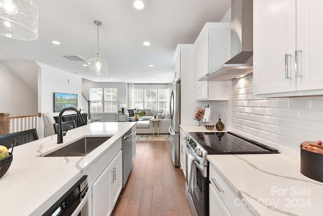 kitchen featuring sink, white cabinetry, stainless steel appliances, wall chimney exhaust hood, and decorative light fixtures