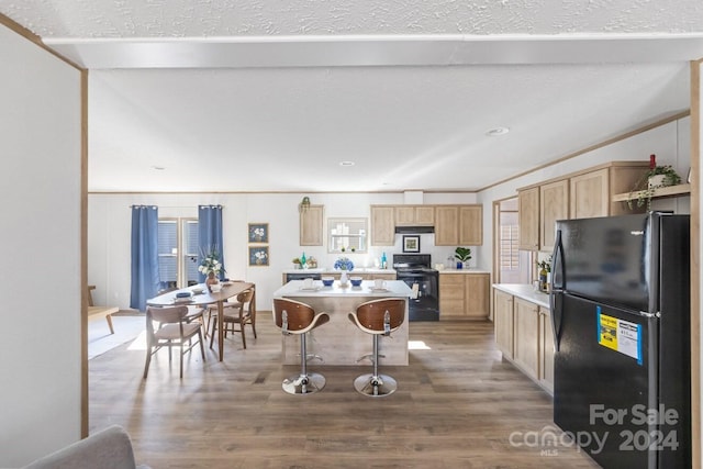 kitchen with wood-type flooring, black appliances, a breakfast bar, and a center island