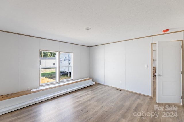 empty room with a baseboard heating unit, light hardwood / wood-style floors, ornamental molding, and a textured ceiling