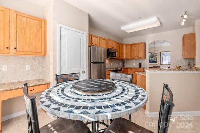 kitchen with decorative backsplash, light stone countertops, stainless steel appliances, and light tile patterned floors