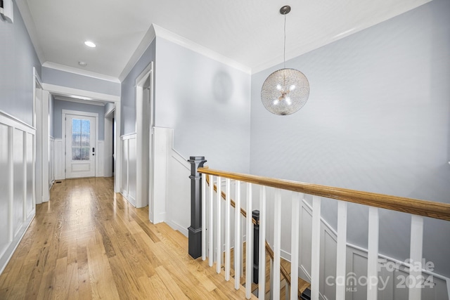 corridor with light hardwood / wood-style floors, crown molding, and an inviting chandelier