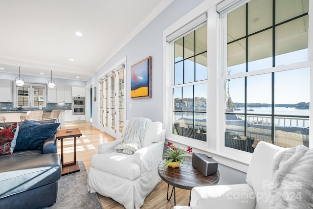 living room with ornamental molding, light hardwood / wood-style flooring, and a water view