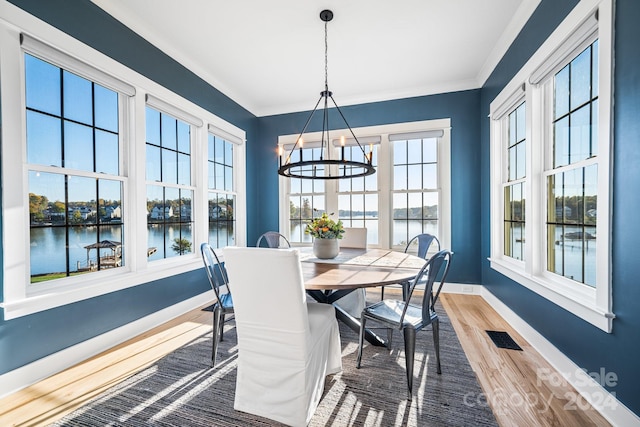 dining space featuring ornamental molding, wood-type flooring, a water view, and an inviting chandelier