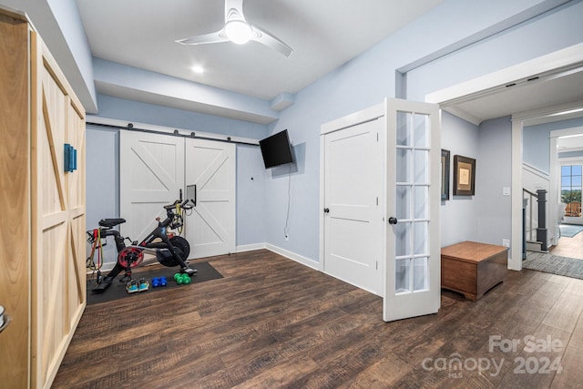 workout room featuring a barn door, dark hardwood / wood-style floors, and ceiling fan