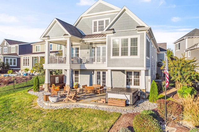 rear view of property featuring a patio, a hot tub, a lawn, and a balcony