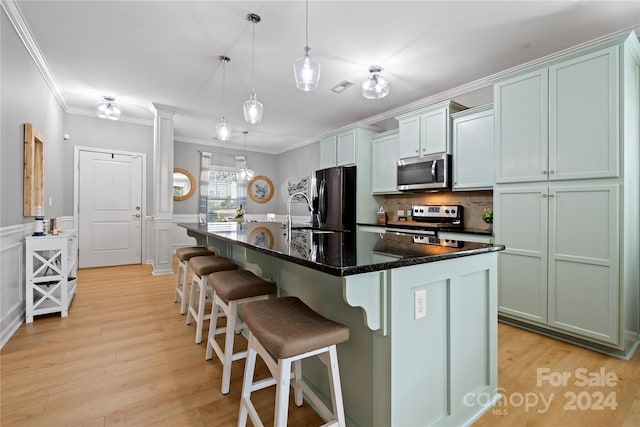 kitchen featuring hanging light fixtures, stainless steel appliances, crown molding, light hardwood / wood-style flooring, and a kitchen island with sink