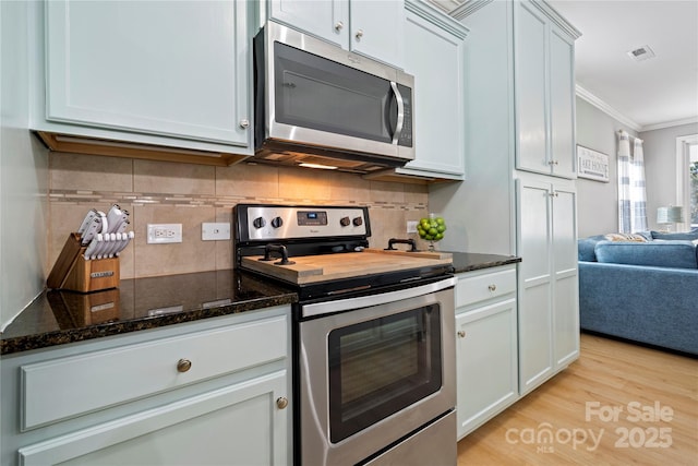 kitchen featuring light wood finished floors, visible vents, dark stone countertops, stainless steel appliances, and crown molding