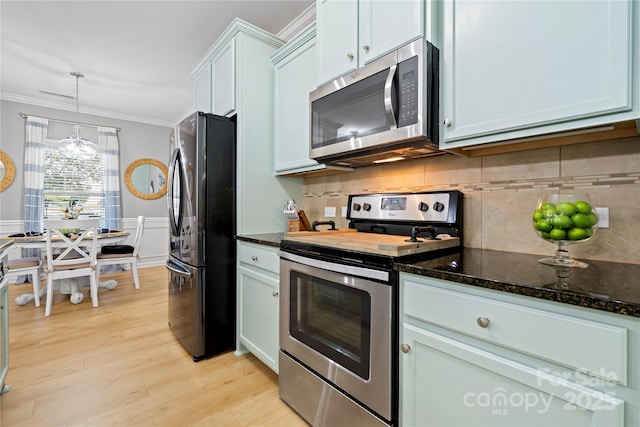 kitchen featuring a wainscoted wall, crown molding, light wood finished floors, appliances with stainless steel finishes, and dark stone countertops