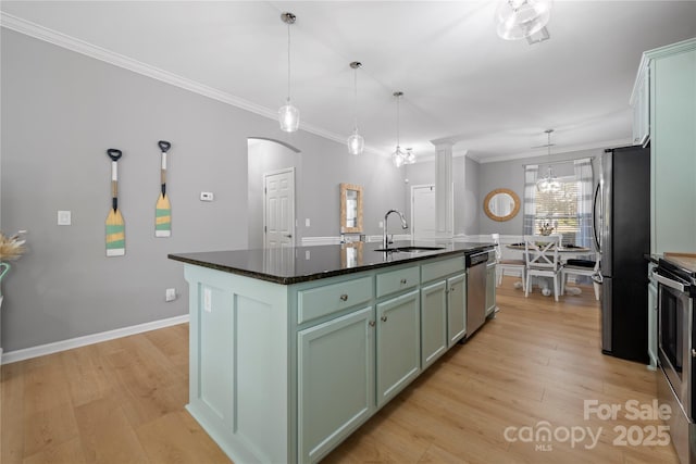 kitchen with arched walkways, an island with sink, light wood-style flooring, appliances with stainless steel finishes, and a sink