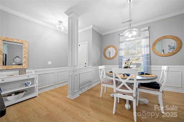 dining room with light wood-style floors, wainscoting, crown molding, and ornate columns