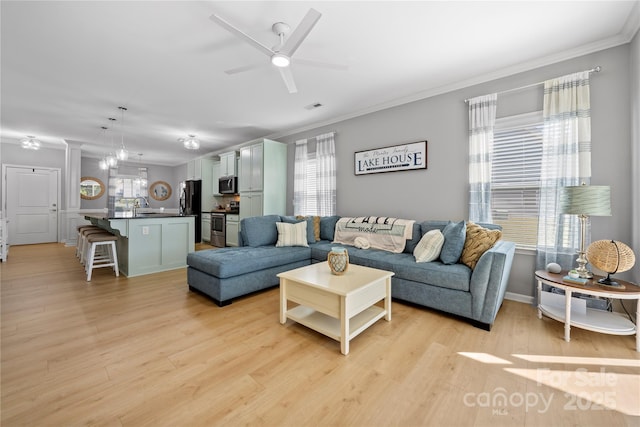 living area with crown molding, visible vents, light wood-style flooring, a ceiling fan, and ornate columns