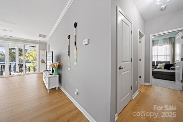 corridor with light wood-style flooring, crown molding, visible vents, and a wealth of natural light