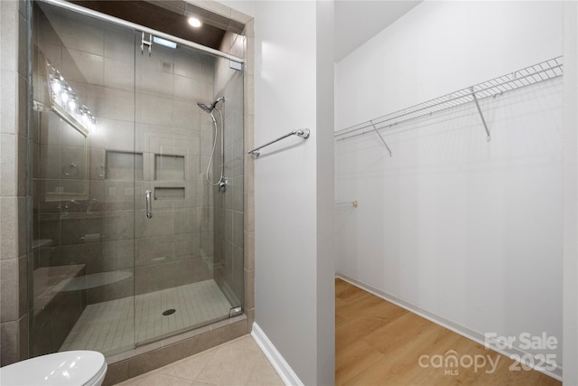 bathroom featuring a stall shower, a walk in closet, toilet, and wood finished floors