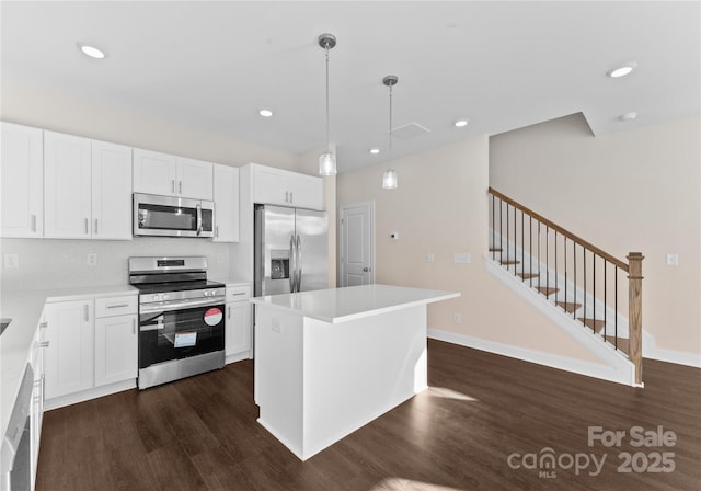 kitchen with appliances with stainless steel finishes, white cabinetry, a kitchen island, and pendant lighting