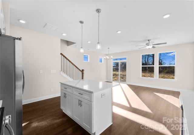 kitchen featuring ceiling fan with notable chandelier, hanging light fixtures, stainless steel fridge, a kitchen island, and white cabinetry