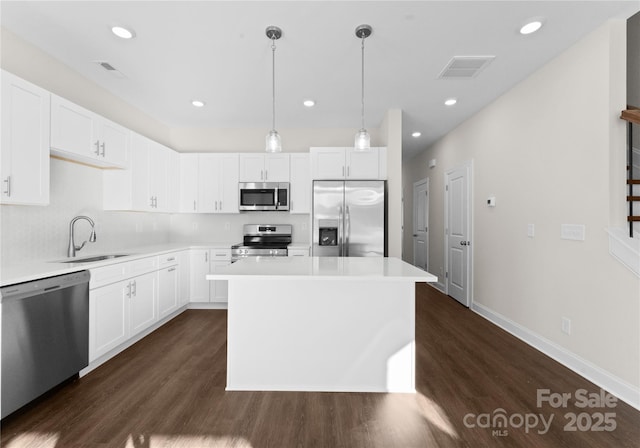 kitchen with appliances with stainless steel finishes, sink, pendant lighting, white cabinetry, and a kitchen island