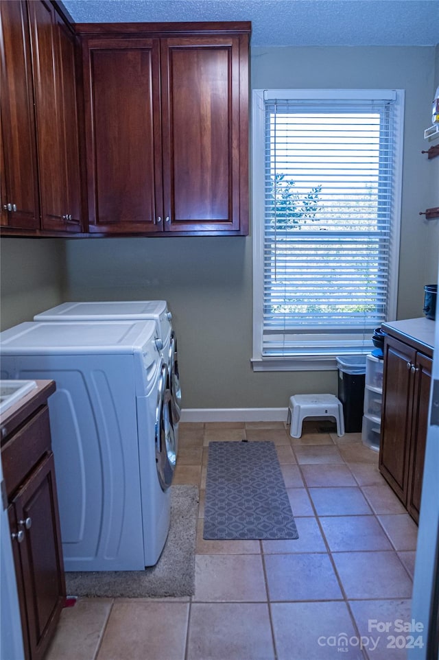 laundry area featuring a textured ceiling, washing machine and dryer, light tile patterned floors, and cabinets