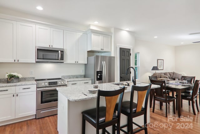 kitchen with a kitchen island with sink, a breakfast bar area, white cabinetry, appliances with stainless steel finishes, and light hardwood / wood-style floors