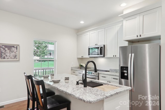 kitchen with white cabinets, hardwood / wood-style floors, light stone countertops, a kitchen island with sink, and stainless steel appliances