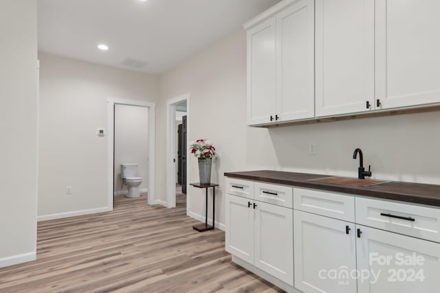 bar with wooden counters, sink, white cabinets, and light hardwood / wood-style floors