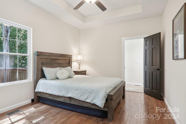 bedroom with ceiling fan, a raised ceiling, and light wood-type flooring