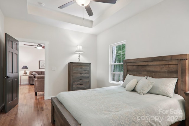 bedroom with ceiling fan, a raised ceiling, and hardwood / wood-style floors