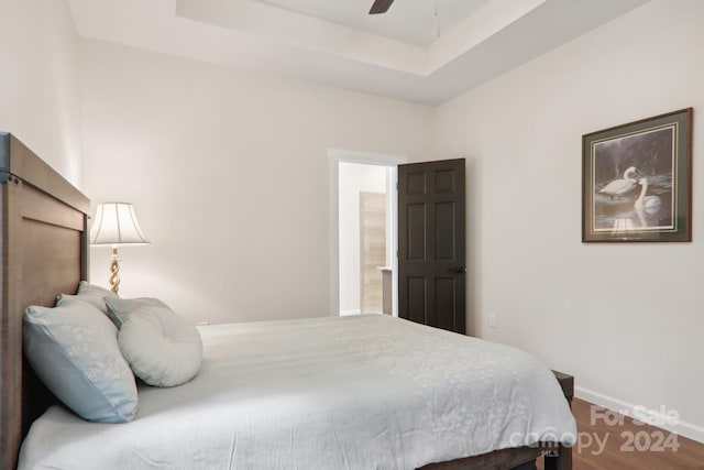 bedroom with ceiling fan, wood-type flooring, and a tray ceiling