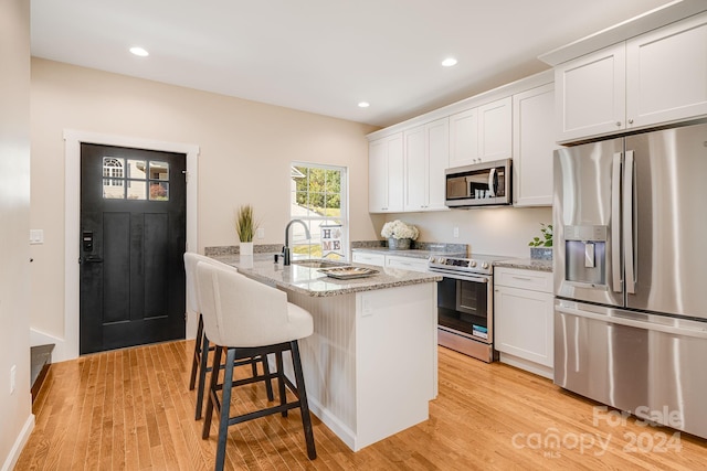 kitchen with a center island with sink, white cabinets, and stainless steel appliances