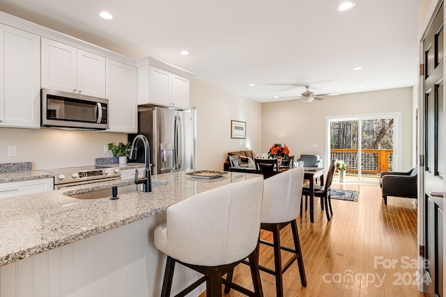 kitchen with white cabinets, a kitchen breakfast bar, stainless steel appliances, and light hardwood / wood-style floors