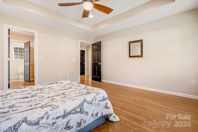 bedroom with light hardwood / wood-style floors, a raised ceiling, ceiling fan, and ensuite bathroom