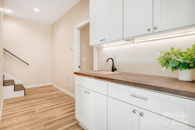 bar with sink, white cabinets, wooden counters, and light hardwood / wood-style flooring