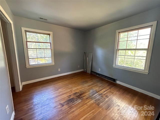 empty room with baseboard heating, hardwood / wood-style floors, and a healthy amount of sunlight