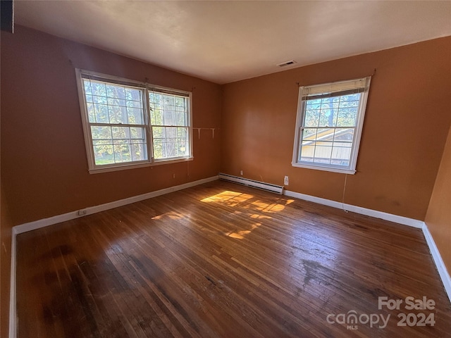 unfurnished room featuring a baseboard heating unit, dark hardwood / wood-style floors, and plenty of natural light