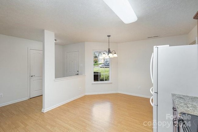 unfurnished dining area with an inviting chandelier, light hardwood / wood-style flooring, and a textured ceiling