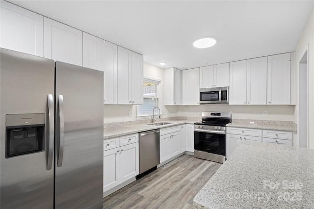 kitchen featuring appliances with stainless steel finishes, light stone counters, sink, light hardwood / wood-style flooring, and white cabinetry